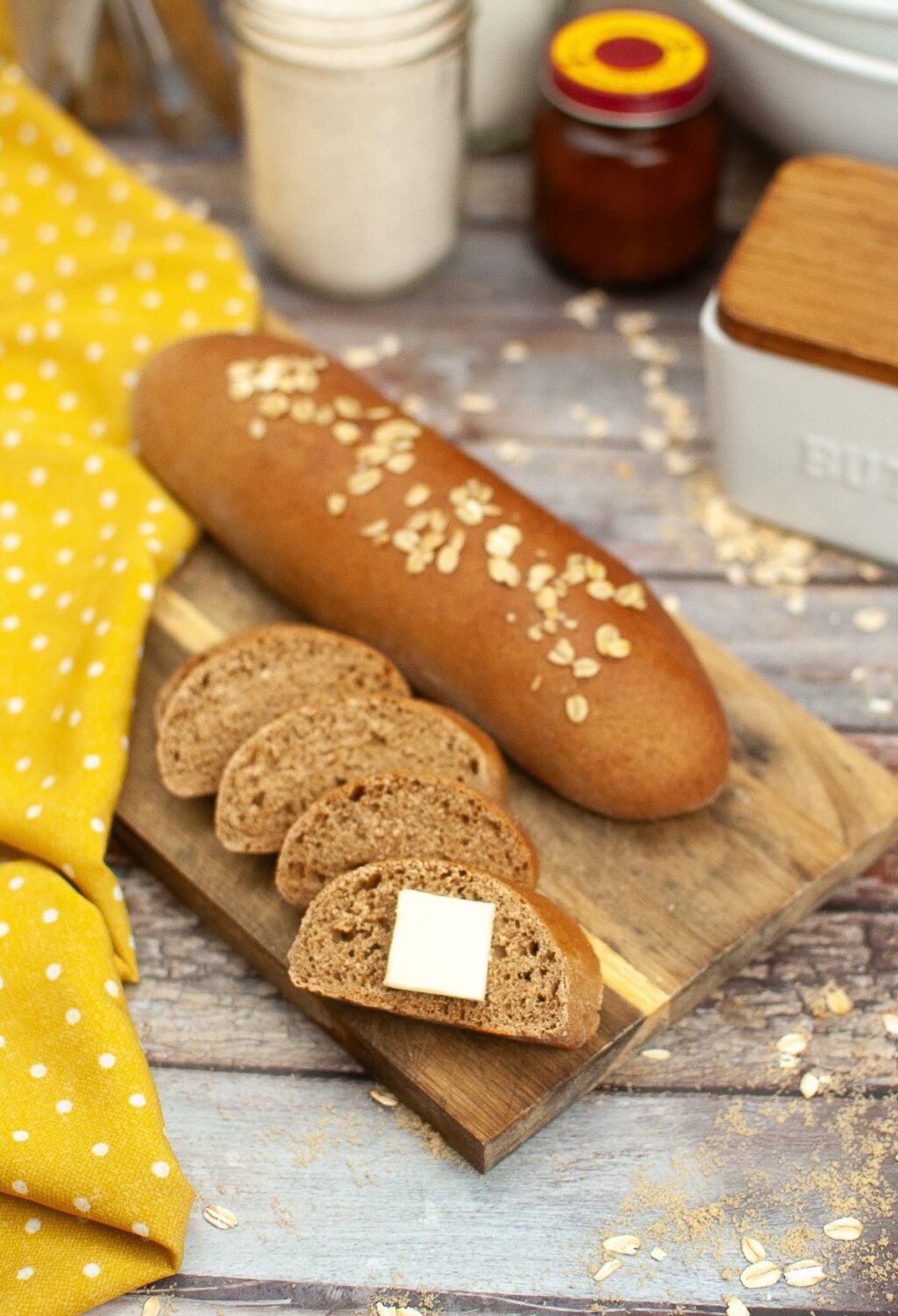 A loaf of bread on a cutting board with butter and oats.