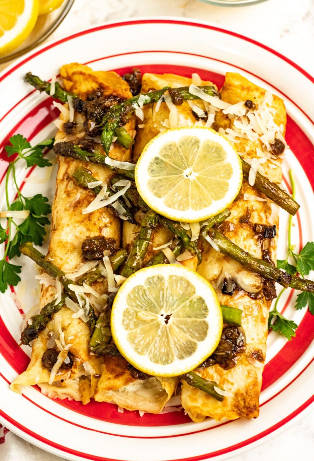 Enchiladas with asparagus and lemon on a red and white plate.