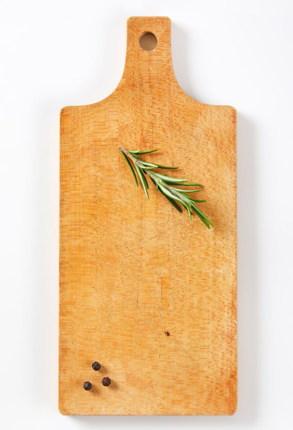A wooden cutting board with a rosemary sprig on it.