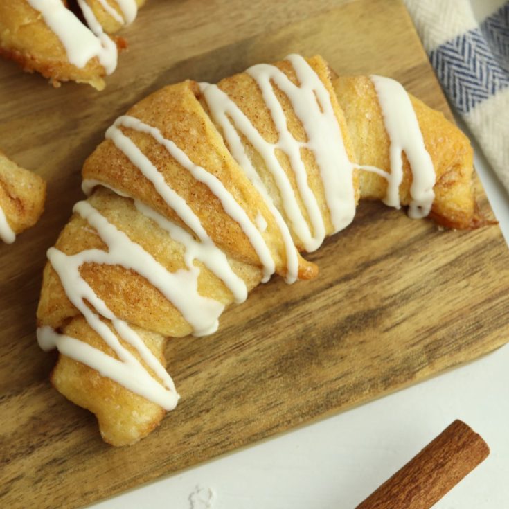 Cinnamon roll crescents on a wooden cutting board.