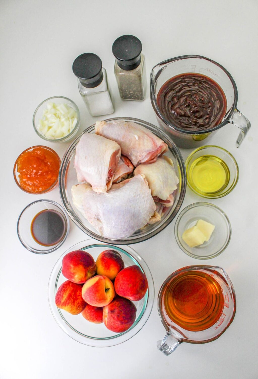 The ingredients for a chicken and peach dish are laid out on a white surface.