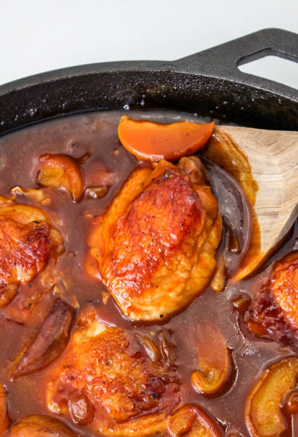 A skillet full of chicken in a sauce with a wooden spoon.