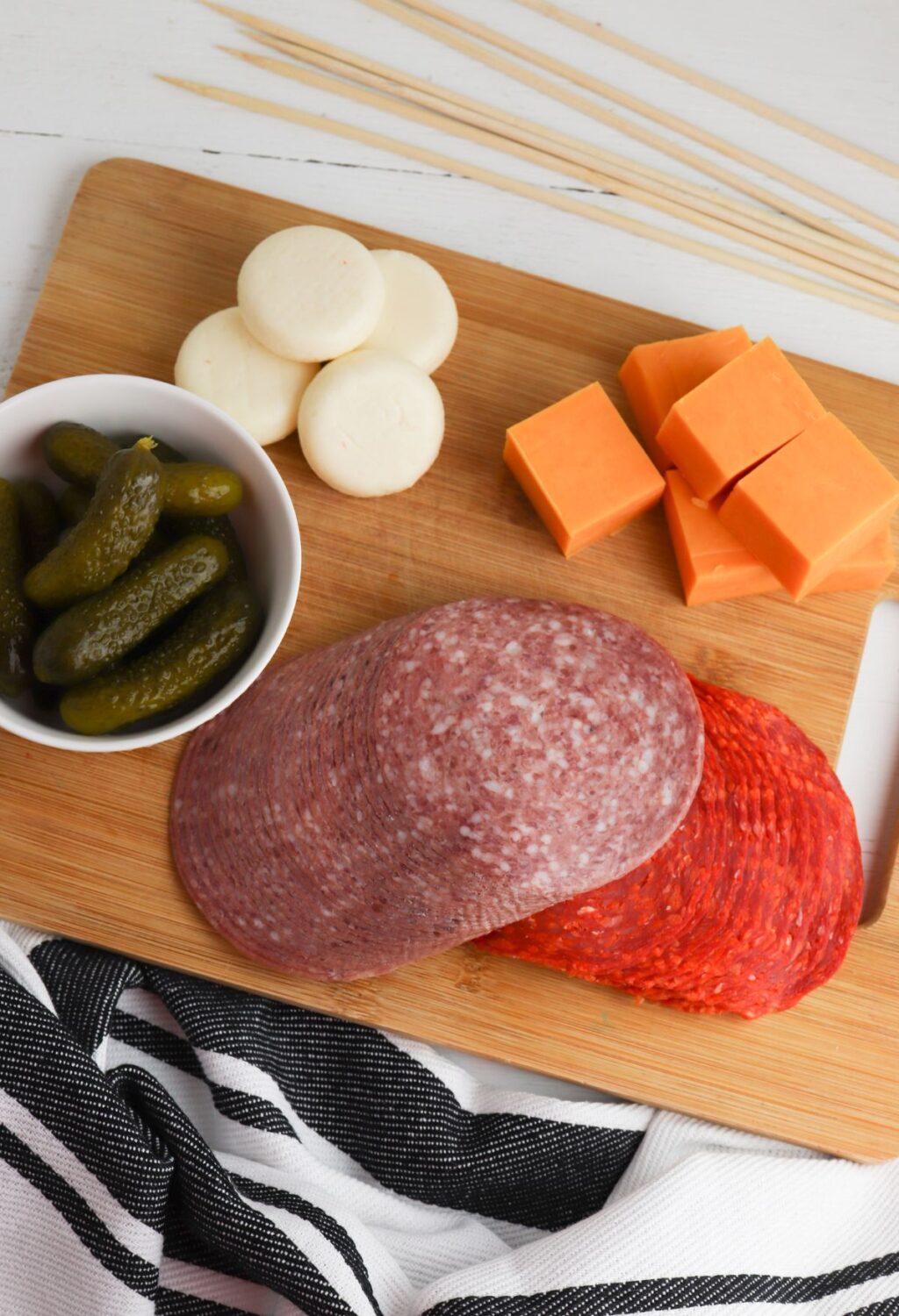A wooden cutting board with meat, cheese and pickles.