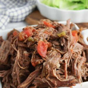 Slow cooker pulled beef with peppers and tomatoes in a white dish.