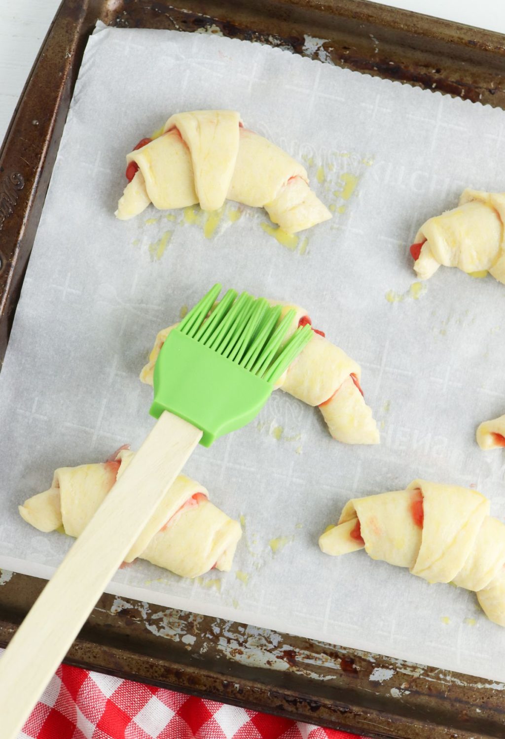 A green spatula is used to brush dough onto a baking sheet.