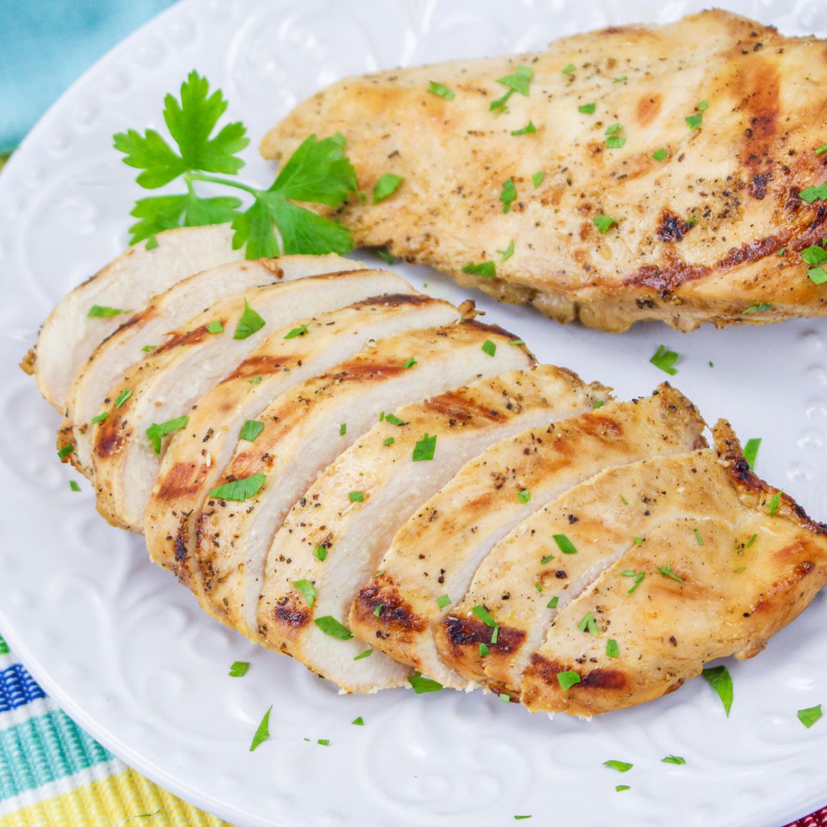 Grilled chicken breasts on a white plate with parsley.