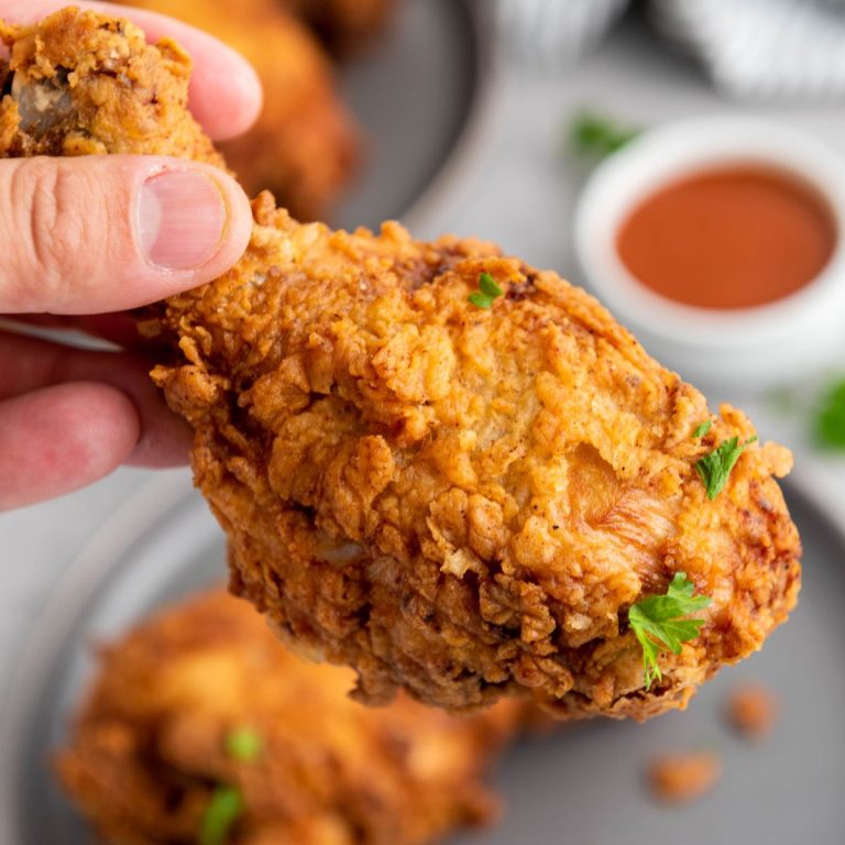 A hand holding fried chicken on a plate.