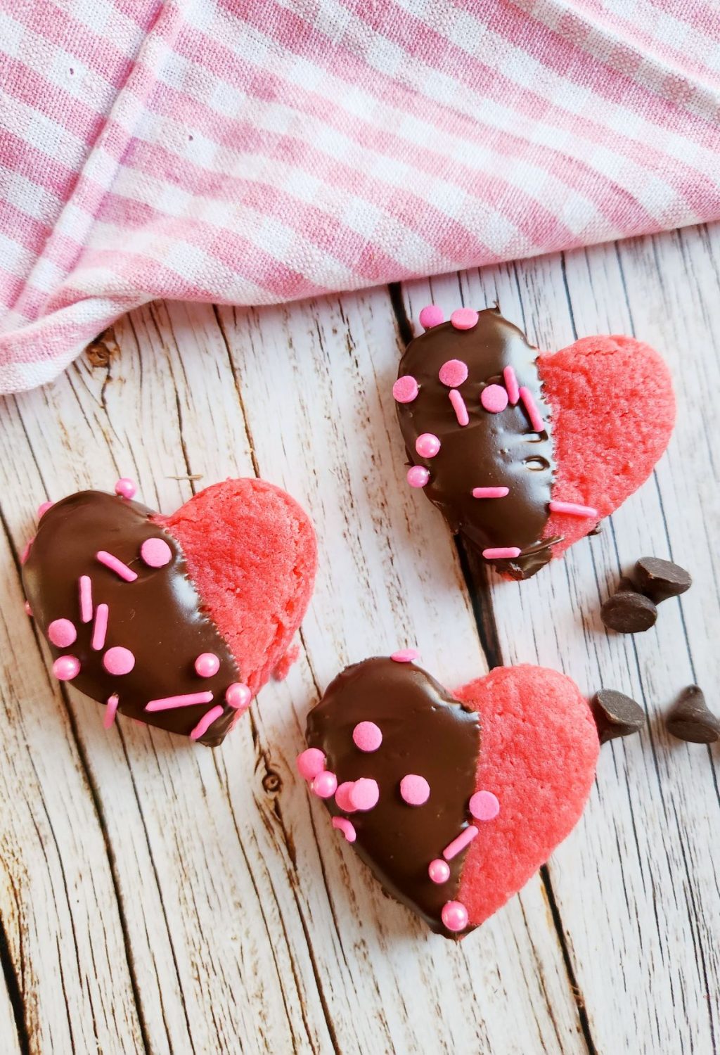 Chocolate heart cookies with pink sprinkles on a wooden table.