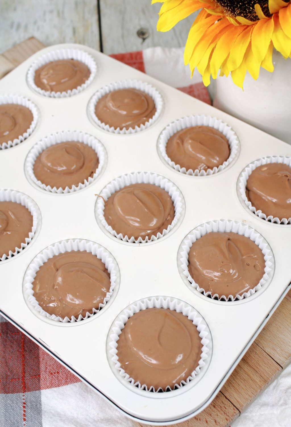 Chocolate cupcakes in a muffin tin with sunflowers.