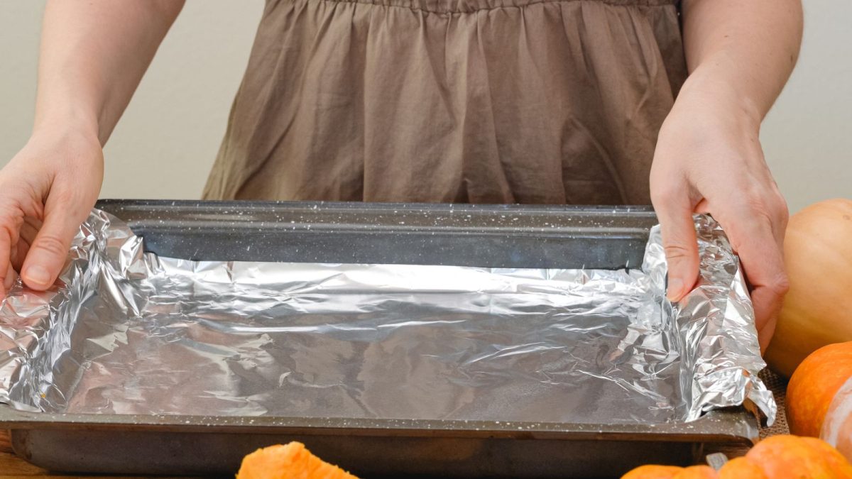 Why You Should Think Twice Before Lining Your Oven With Aluminum Foil 1 woman lining baking sheet with aluminum foil