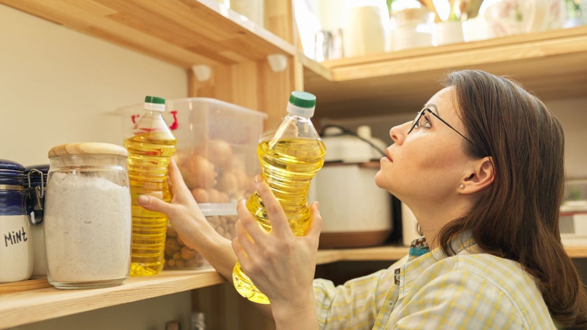 Food storage, wooden shelf in pantry with products. Woman taking food, sunflower oil for cooking