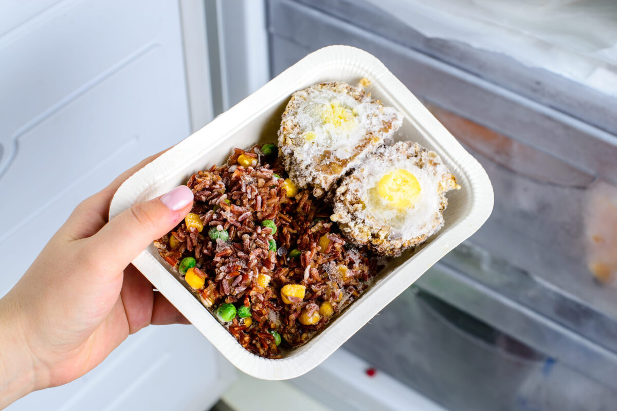 8 Freezer Foods You Should Toss Immediately for Your Health and Safety 3 frozen food from the freezer in the female hand, Woman placing container with frozen ready meals in refrigerator