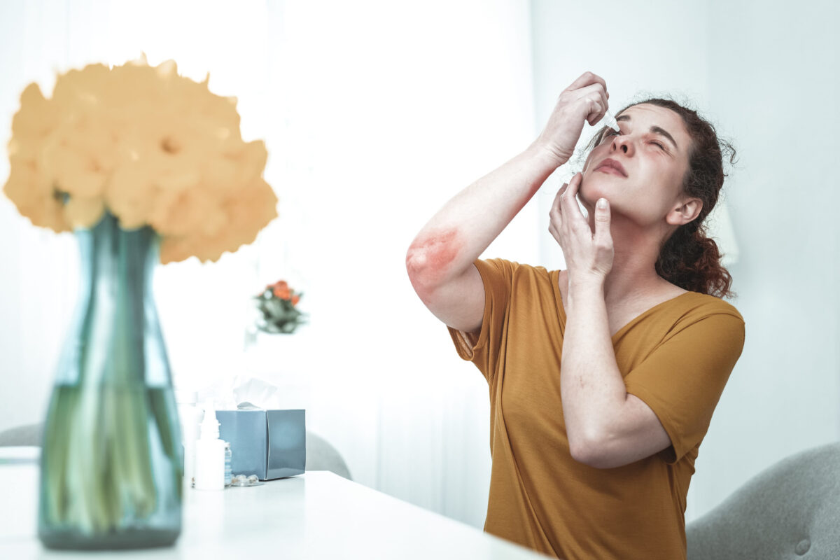 The 6 Health Hazards of Genetically Modified Foods 2 Eye drops. Young curly red-haired woman using eye drops while having allergy to flowers