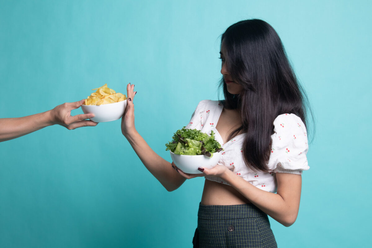 The Adverse Effects of a Vegan Diet and Understanding the Potential Risks 1 Young Asian woman with salad say no to potato chips on cyan color background