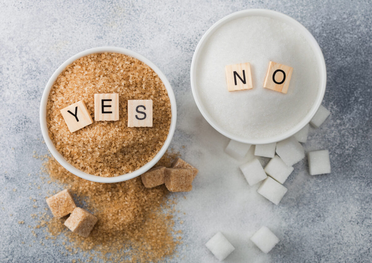 The 8 Worst Foods for Your Hormonal Health, And How They’re Affecting Your Mood 1 White bowl plates of natural brown and white refined sugar and cubes on light background.Yes and no letters. Healthy and unhealthy concept.Top view