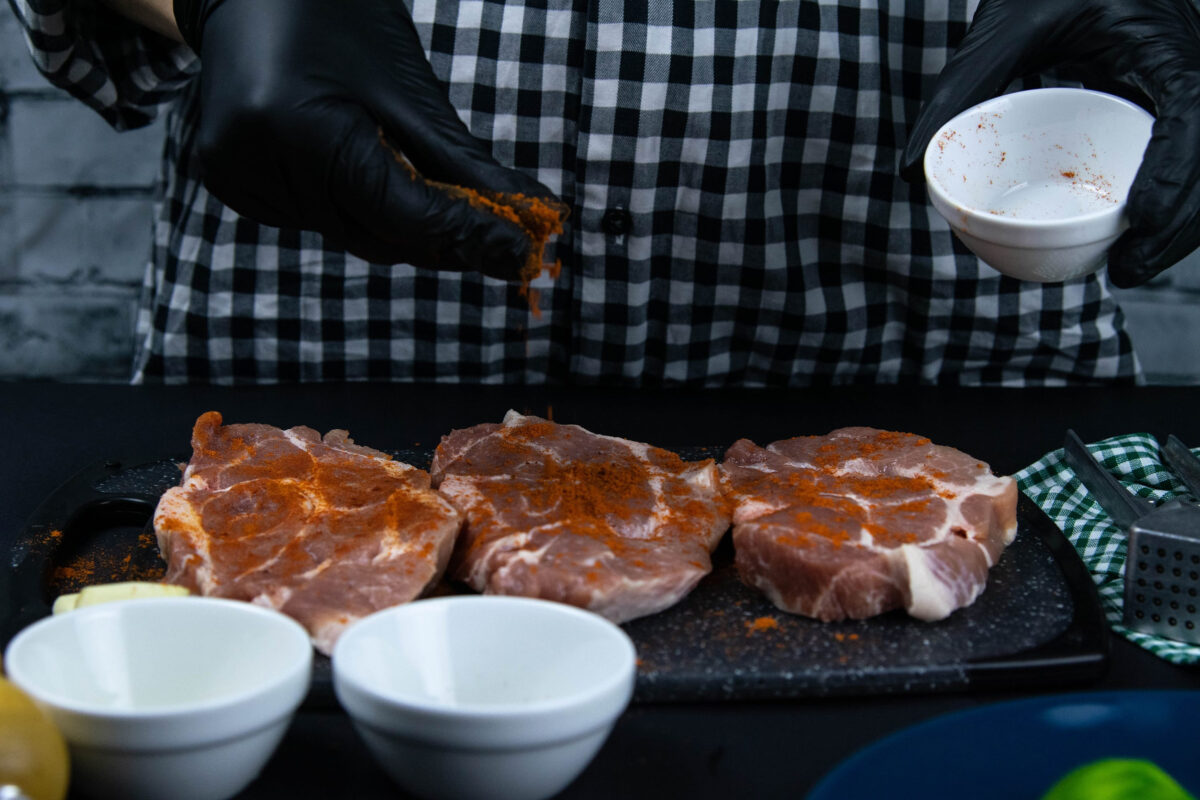 10 Ways You Are Cooking Meat Wrong and How to Fix Them 3 A chef in black gloves sprinkled with red pepper a raw pork