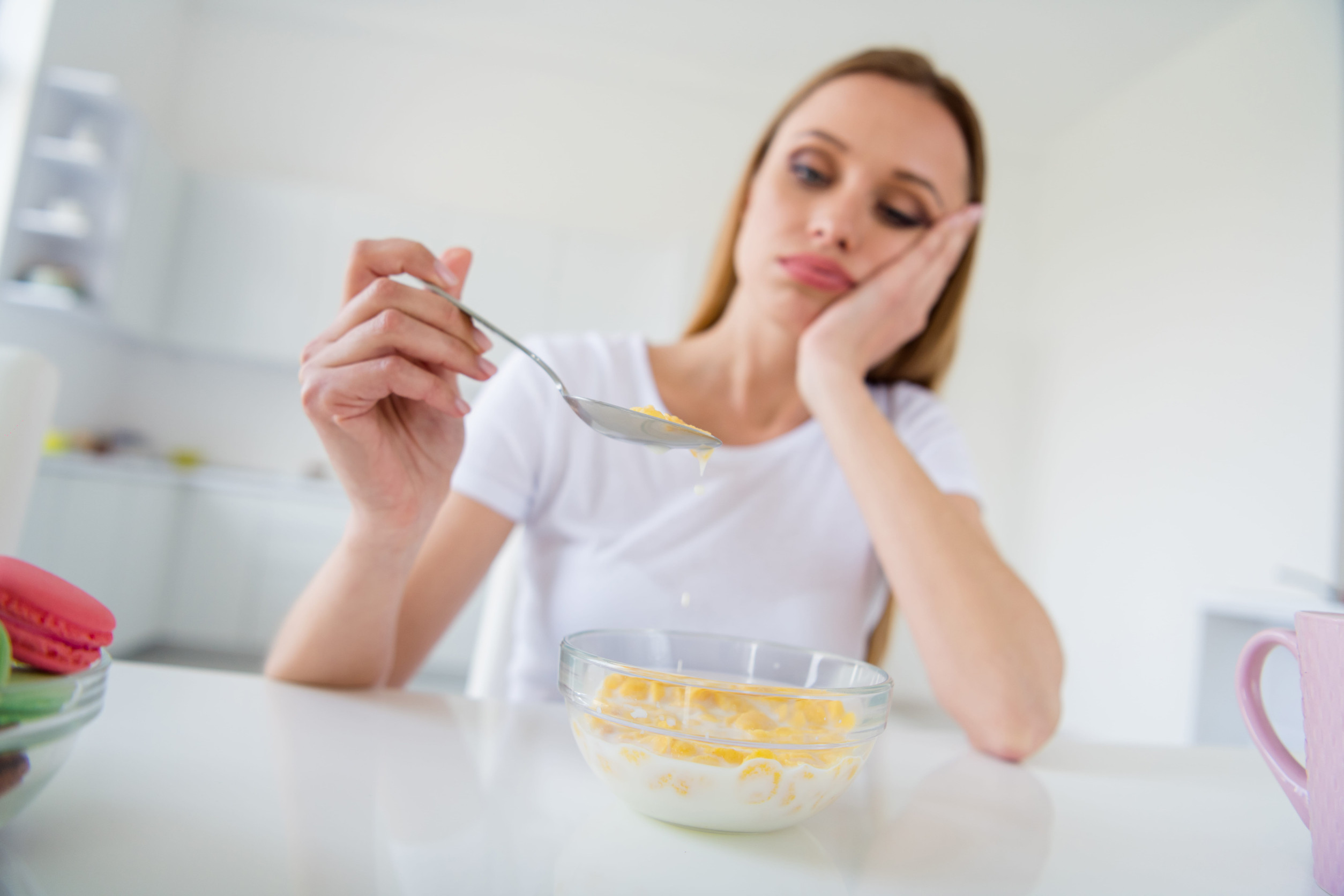 Photo of beautiful blond upset housewife holding spoon don't want eat milk, breakfast cornflakes tired of dieting bored sitting table white light kitchen indoors