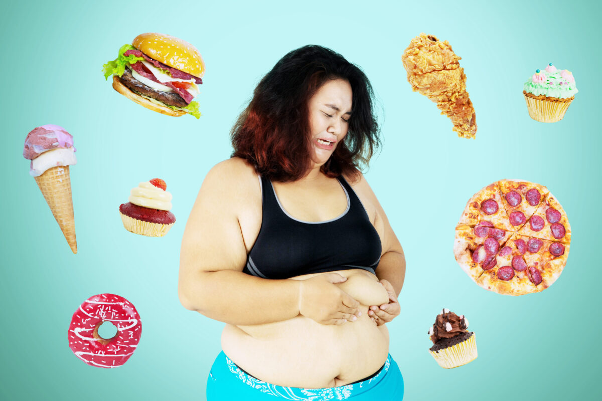 The 6 Truths About Sugar-Free Foods and Why They Could Be Worse Than You Think 3 Portrait of obese woman looks cry while pinching her belly fat and standing with junk foods background. Diet fail concept