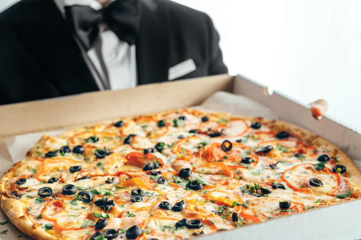 The Most Expensive Pizzas in America 1 A man in a suit and bow tie holds a box of pizza in his hands.