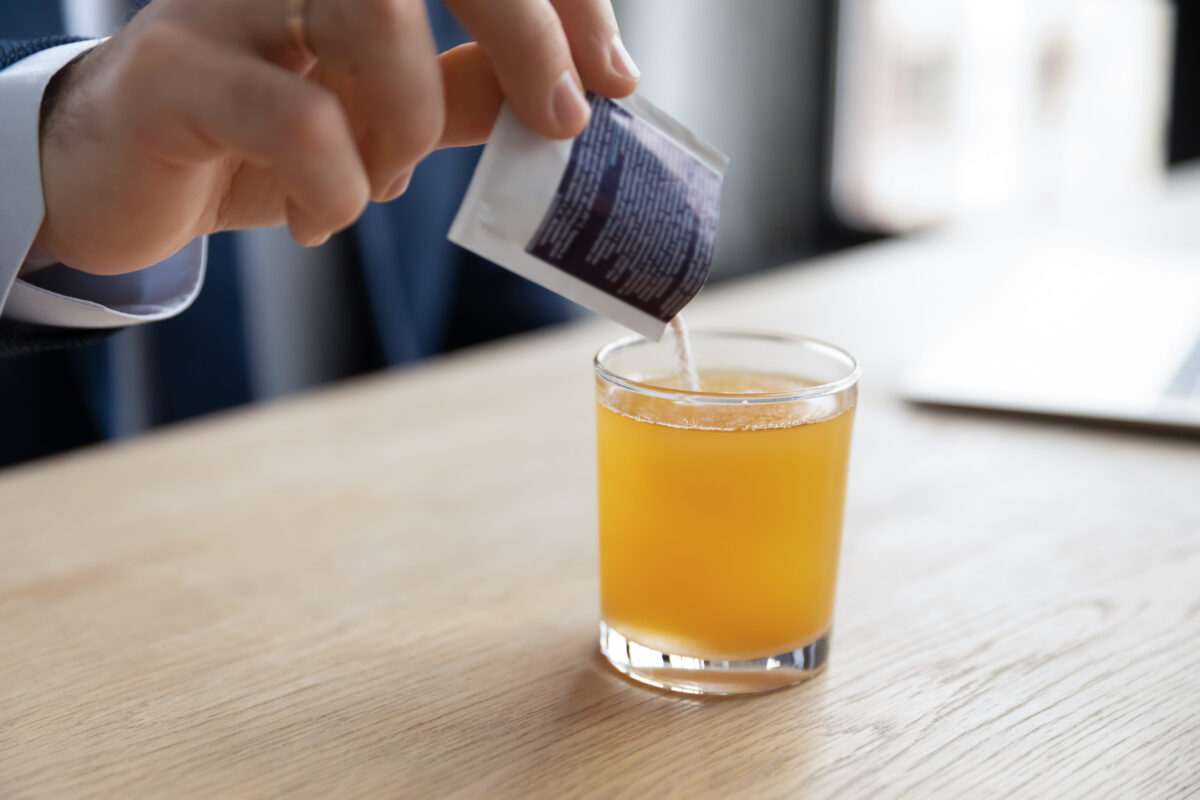 The Hidden Dangers of Juice 1 Close up young businessman pouring soluble anti-influenza orange powder with citrus taste in glass of water, feeling first grippe illness symptoms at workplace or relieving headache with painkiller.