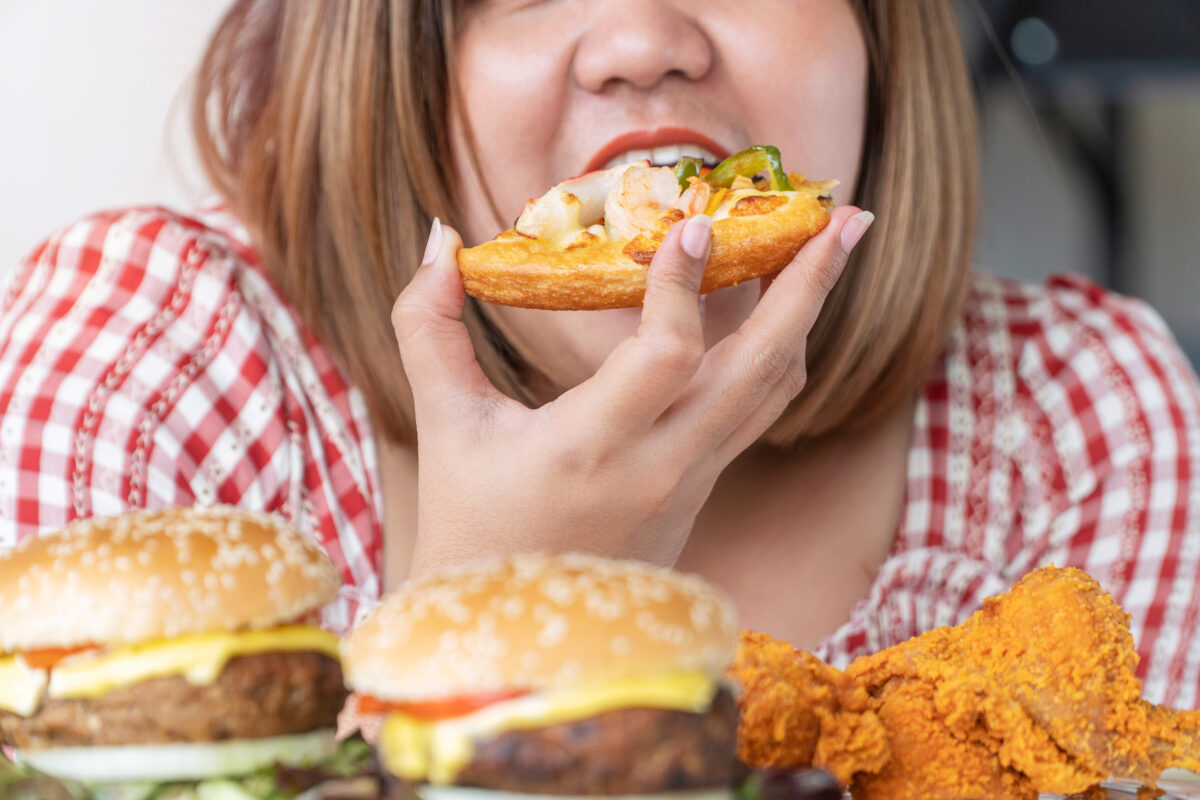 The 10 Worst Foods You Could Eat for Your Skin and What You Should Choose Instead 4 Unhealthy with junk food concept. Hands of oversize fat woman eating pizza with hamburger and chicken fried on table. Close up hungry obese girl tasty fast food meal in own hand.