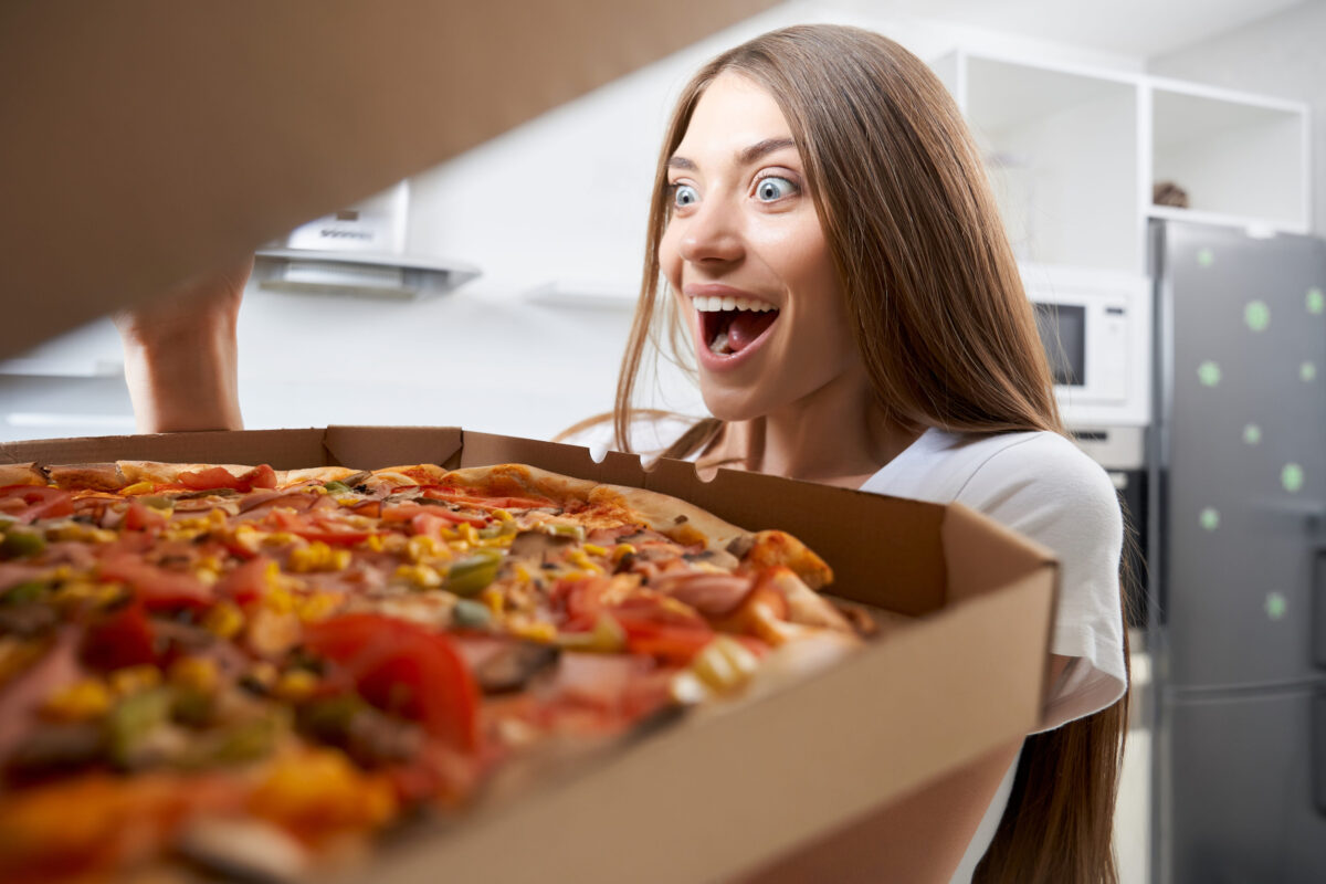 If Calories Didn’t Count, These Are the Foods People Would Recklessly Eat Every Day 1 Happy young woman holding hot pizza in box at home. Concept of tasty pizza