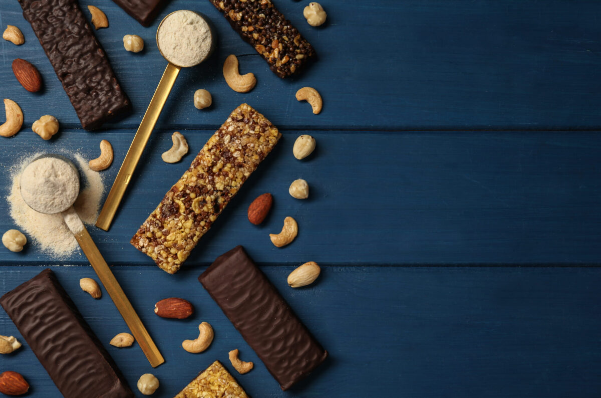 The 6 Truths About Sugar-Free Foods and Why They Could Be Worse Than You Think 2 Different tasty bars, nuts and protein powder on blue wooden table, flat lay. Space for text