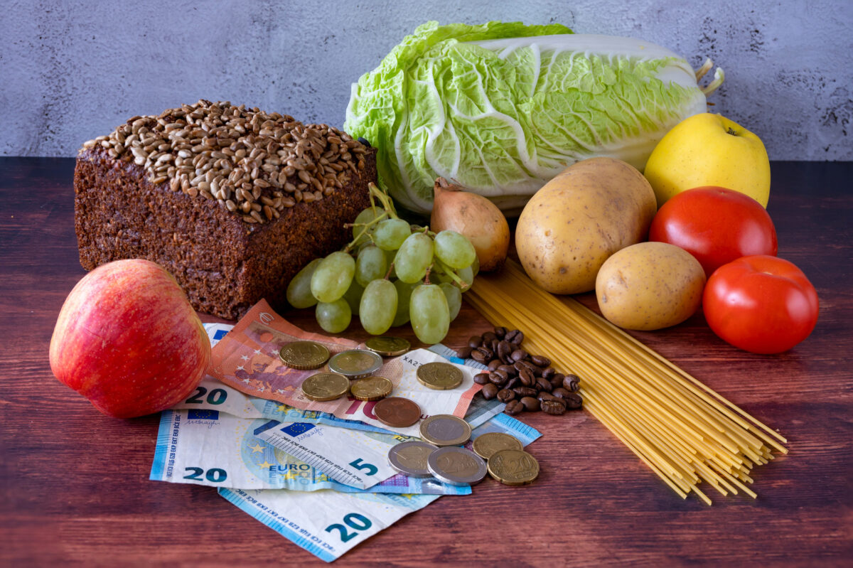 Food lies on a wooden table along with European banknotes and coins symbolizing inflation.