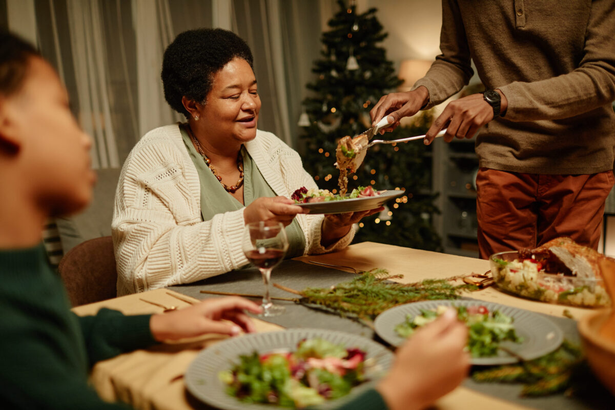 Dietitians Reveal the 8 Common Holiday Habits That Can Cause Unstable Blood Sugar 3 Portrait of happy African-American grandmother enjoying food during Christmas dinner with family