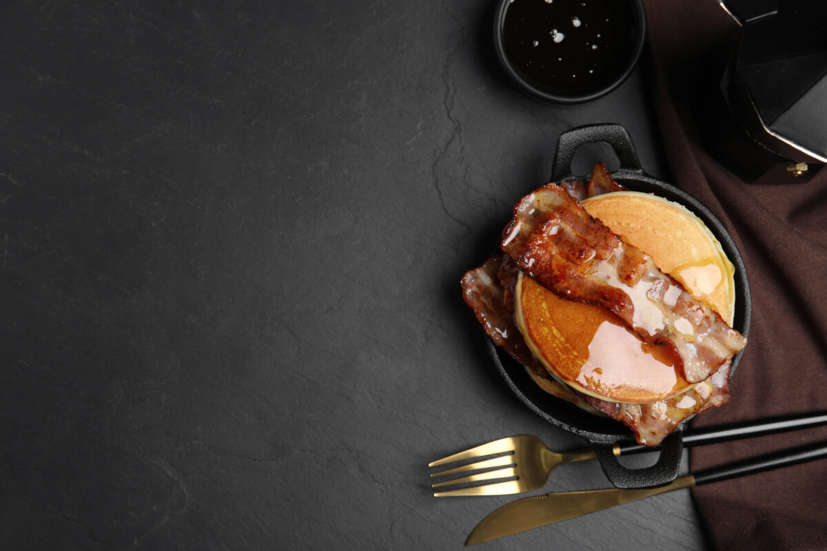 7 Unexpectedly Delicious Food Pairings You Need to Try Right Now 5 Delicious pancakes with maple syrup and fried bacon on black table, flat lay. Space for text