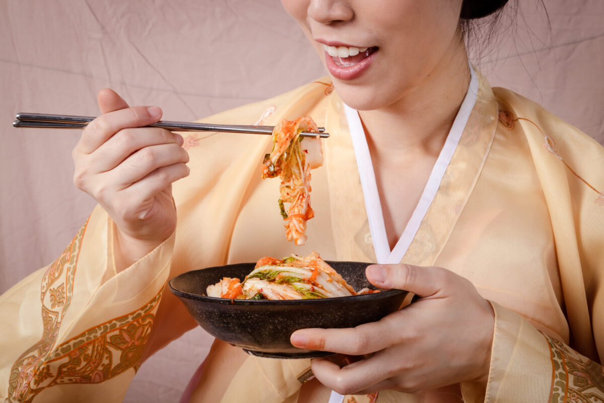 10 Stinky Foods That Are Surprisingly Delicious 3 Asian woman wearing hanbok Hold the chopsticks to taste the kimchi in a tiled bowl. Concept of Korean fermented cooking