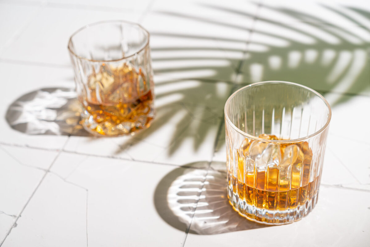 The 8 Worst Foods for Your Bones. What to Avoid for Stronger, Healthier Bones. 2 Whiskey with ice in glasses, white background with hard light, shadows and sun glare, copy space