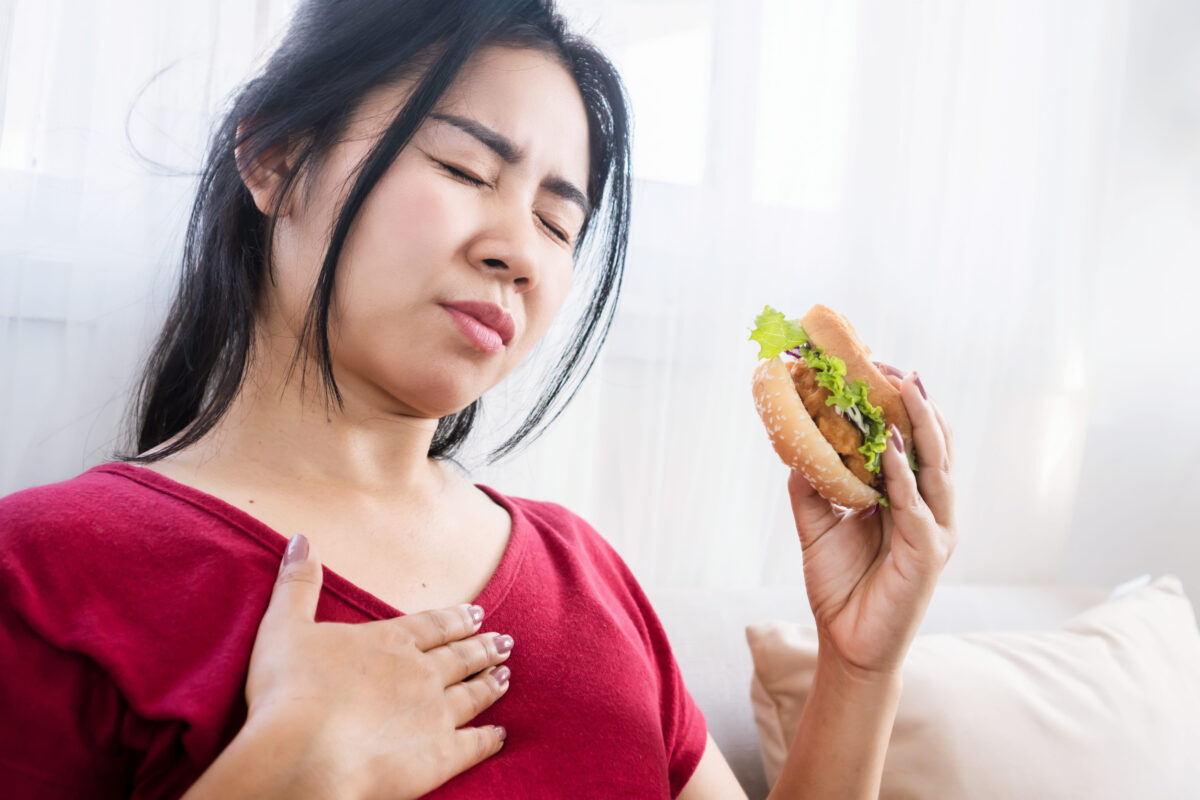10 Early Warning Signs of Stomach Cancer 2 Asian woman having heartburn, acid reflux after eating burger, eating junk food concept
