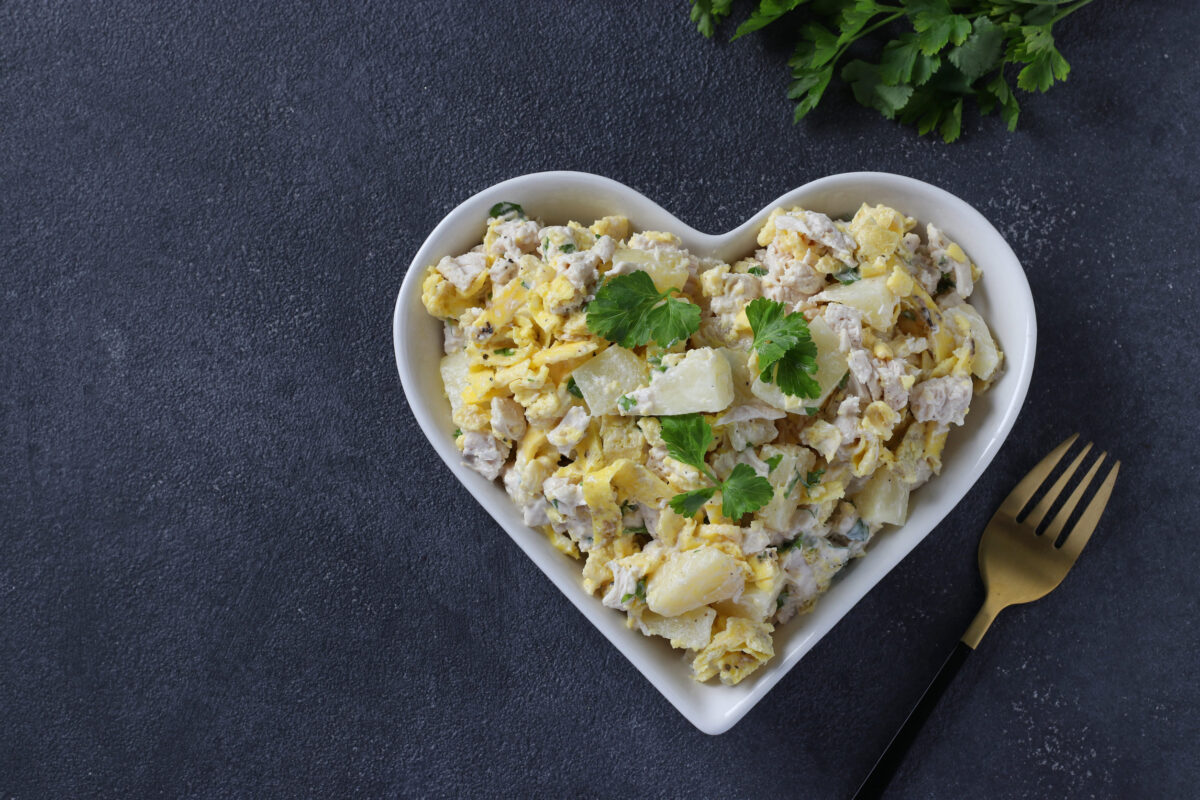 9 Foods You Should Never Bring to a Potluck and What to Bring Instead 2 Salad with pineapple, baked chicken and omelette in heart shaped plate on a dark gray background