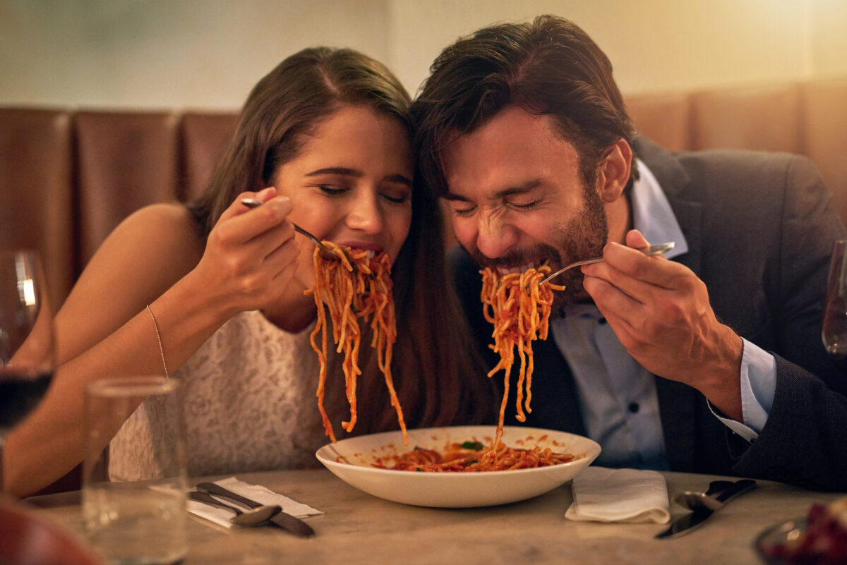 10 The Worst Foods to Eat on a Date 1 Love is all consuming. Shot of a young couple sharing a plate of spaghetti during a romantic dinner at a restaurant.