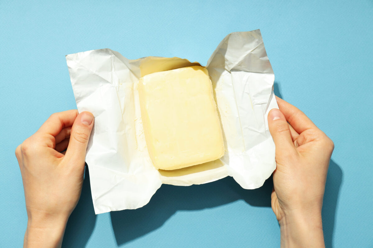 9 Foods You’re Eating That Could Be Poisoning Your Brain 2 Female hands open package with butter on blue background
