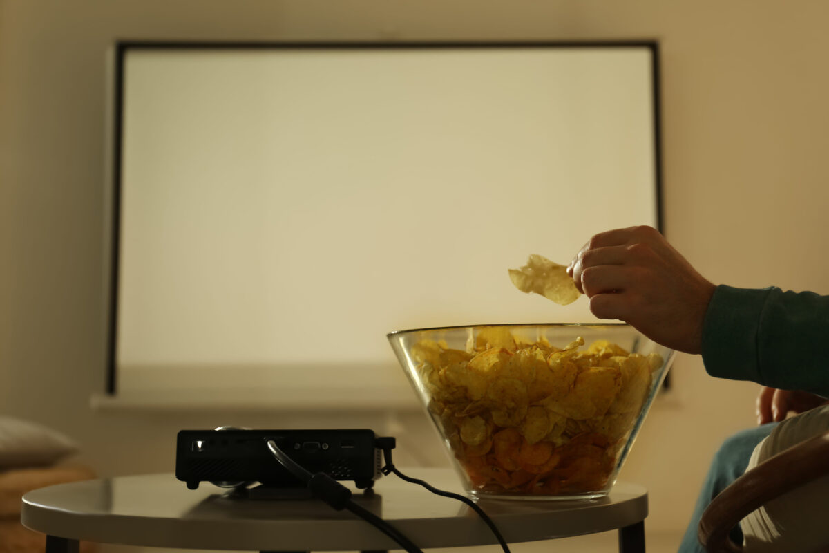 10 Foods That Are Ruining Your Movie Night, and Why You Should Avoid Them 1 Man eating chips while watching movie using video projector at home, closeup