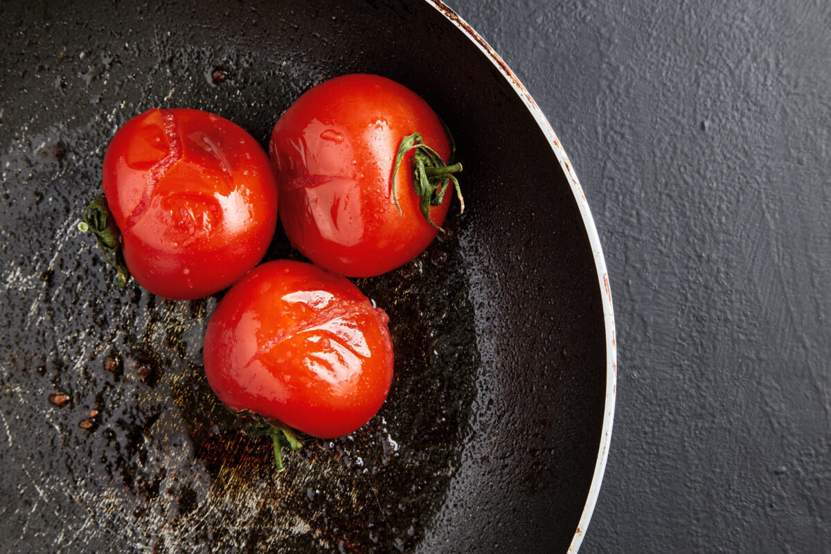 The 10 Foods You Should Never Cook on Cast Iron 1 Grilled baked tomatoes in a black frying pan on a black concrete background. top view with copy space
