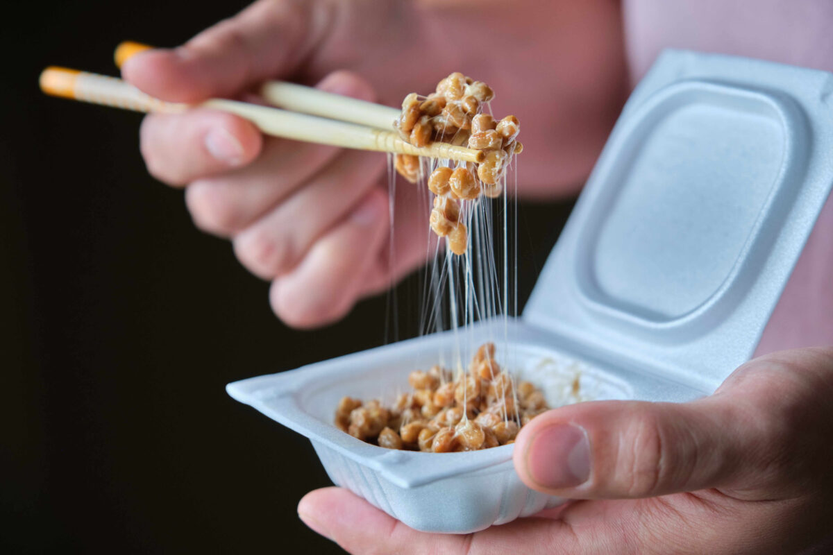 10 Stinky Foods That Are Surprisingly Delicious 2 Close up hand holding natto fermented soy beans with chopsticks in container box. Japanese traditional food.