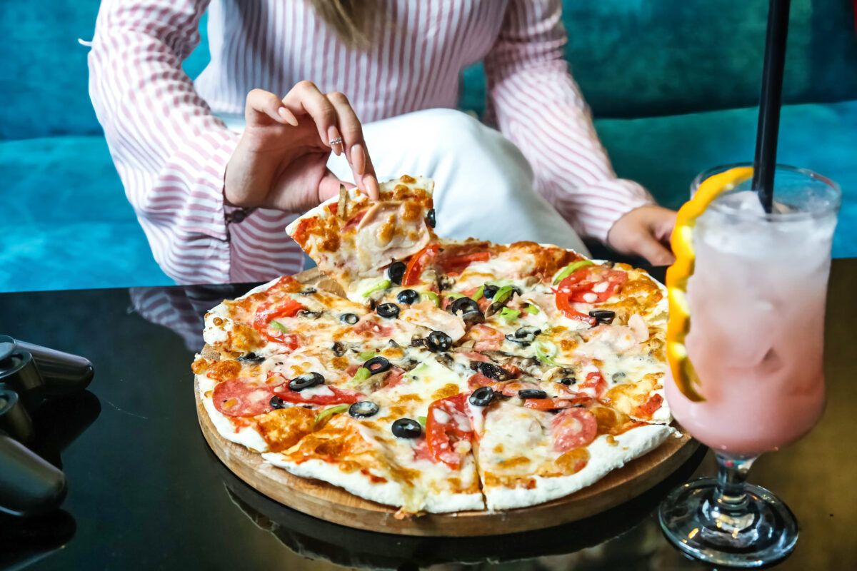 The Most Expensive Pizzas in America 4 A woman sits at a table enjoying a pizza and a drink.