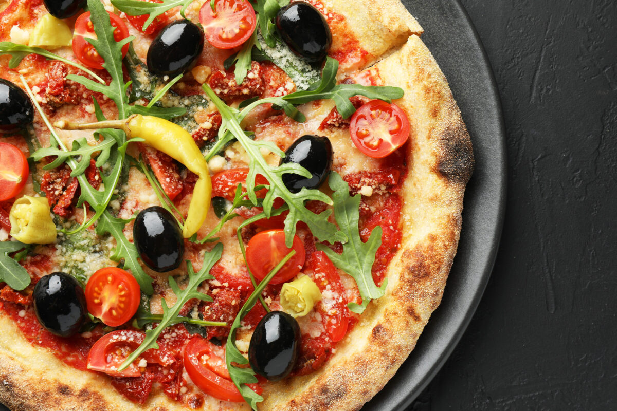 Avoid These 10 Foods on a First Date, They Could Destroy Your Chances 2 Tasty pizza with tomatoes, olives, chili and arugula on black table, top view