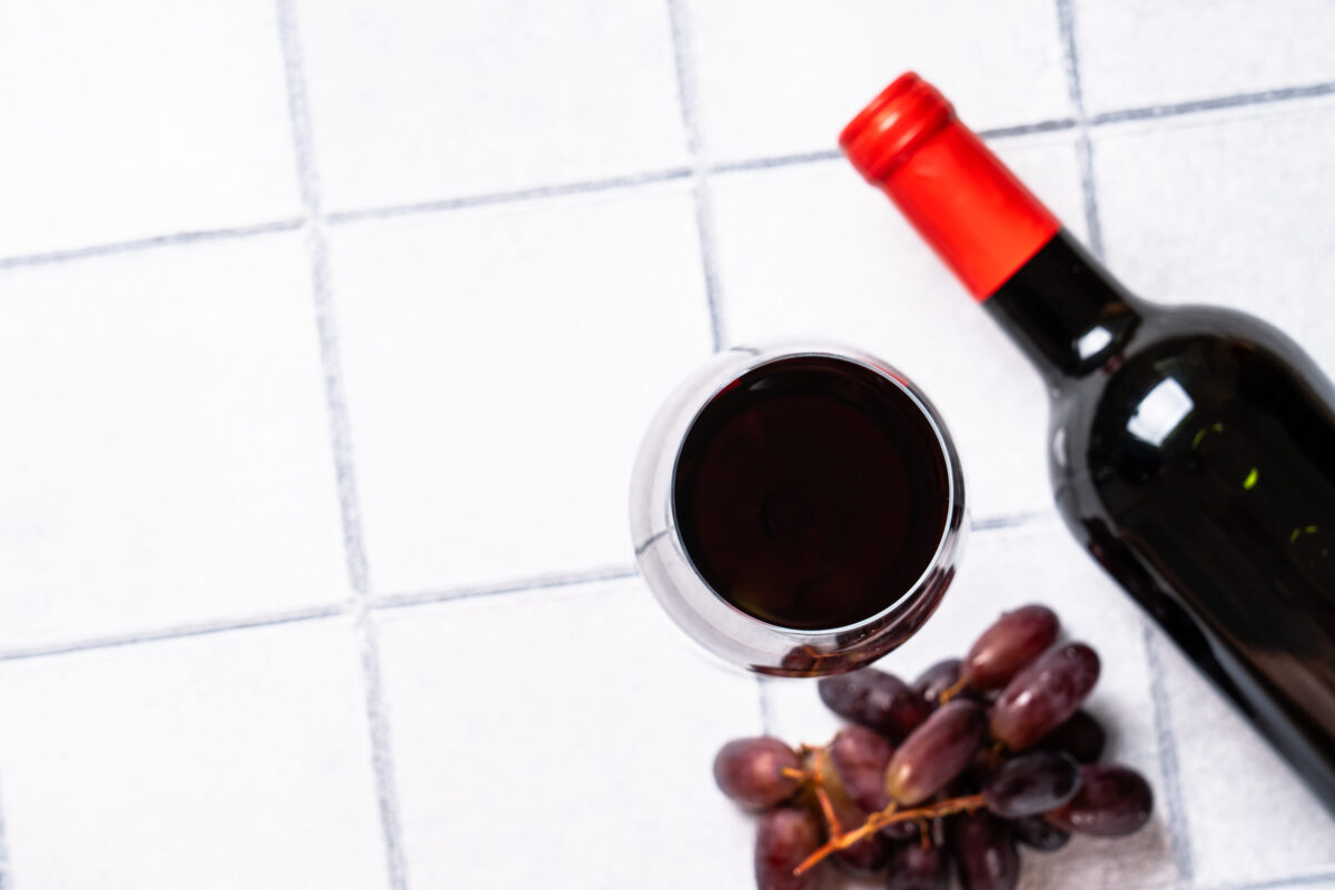 How These 6 “Age Defying” Foods Could Be Harming Your Skin 4 Wine glass on white background. Red wine with grape and wine bottle. Flat lay image with copy space.