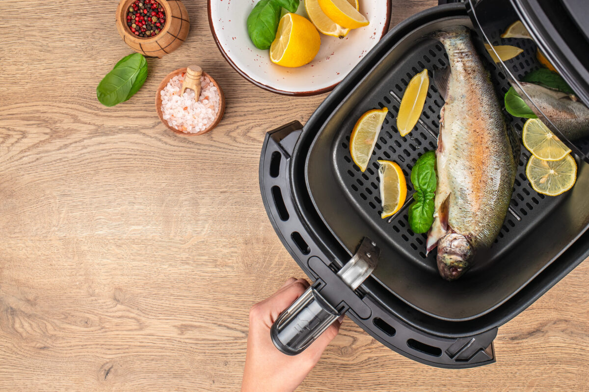 The 7 Foods You Should Never Cook in an Air Fryer 1 Raw fish with lemon slices and basil in air fryer basket, ingredients on wooden table, top view.