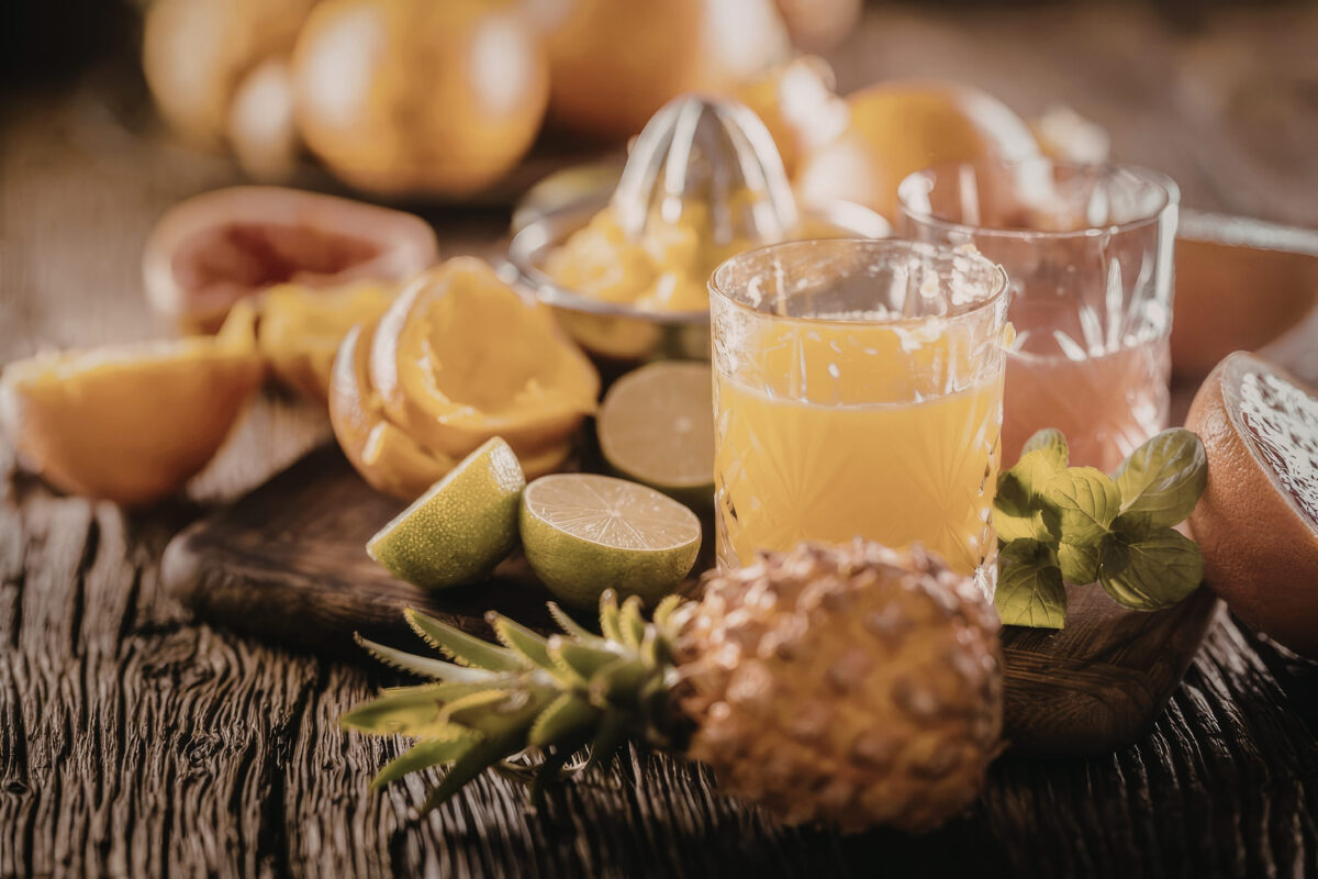 The Truth Behind Overrated Foods 3 Freshly squeezed orange juice is served in a glass with pineapple slices and mint leaves on a rustic wooden table setting.