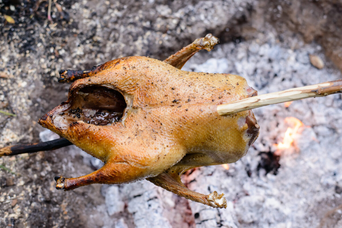 6 Pioneer Foods That Make the Wild West Look Far Less Glamorous 1 Cooking a whole chicken on a single long stick over a campfire with burning coals and hot flames made on the ground, close up view of a delicious crispy brown bird