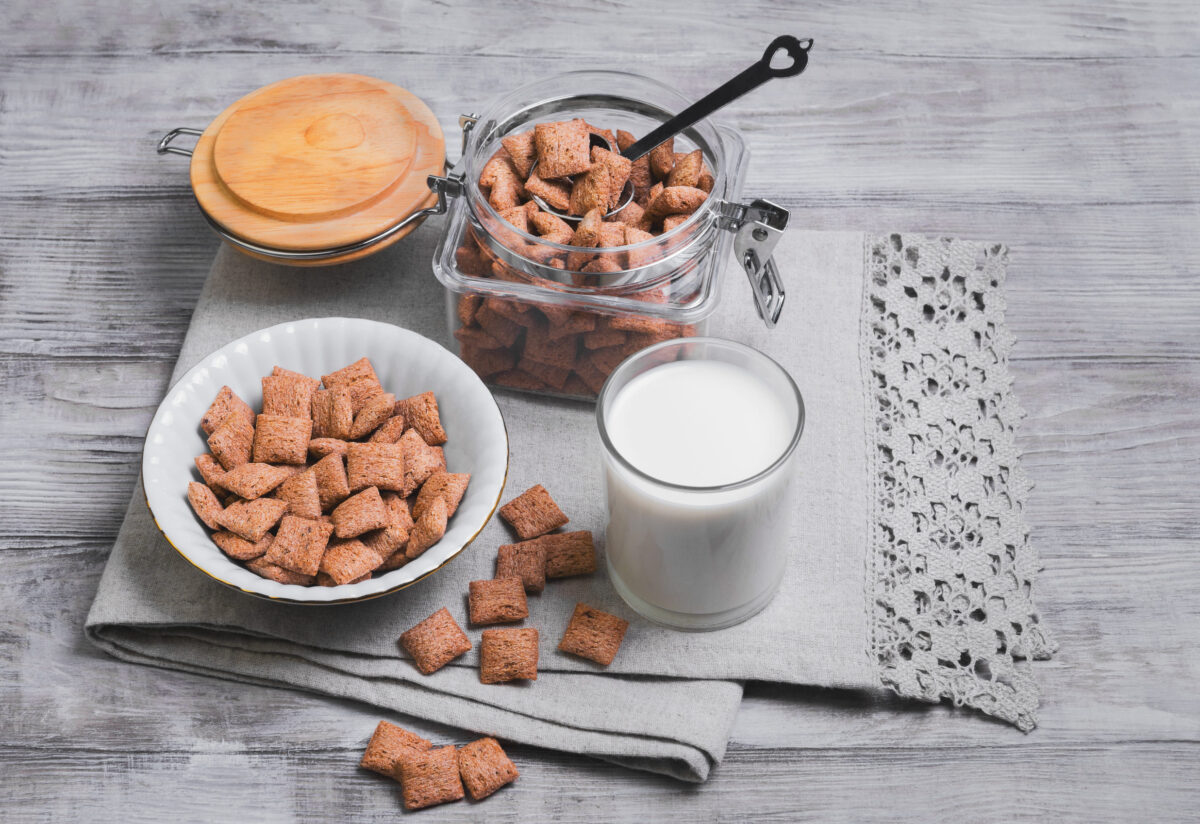 These 9 Food Companies Are Ruining the Environment. Stop Buying From Them 3 Multigrain healthy cereal corn pads chocolate in a white bowl for milk breakfast, glass of milk, cereal bank, cereal is scattered on a table on a light wooden background surface