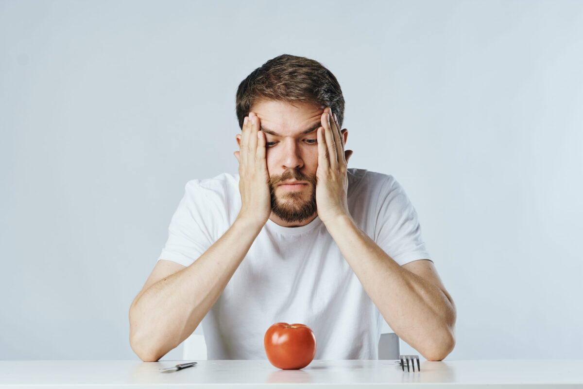 14 Harsh Signs You’re Still Financially Unstable 4 Man with a beard on white isolated background looking at a tomato sitting at a table, diet, vegetables.