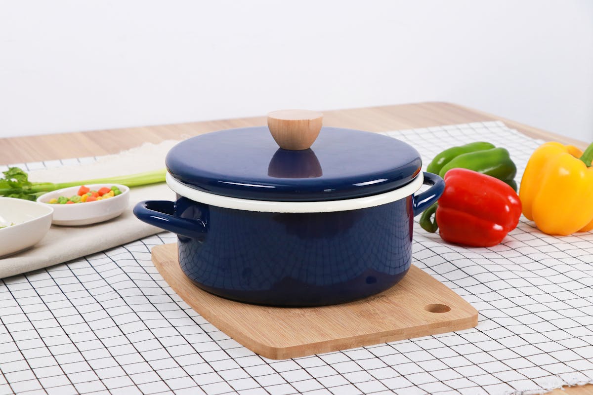 8 Items You Should Stop Storing In Kitchen Cabinets 1 A blue pot on a wooden board surrounded by bell peppers and vegetables on a checkered tablecloth.