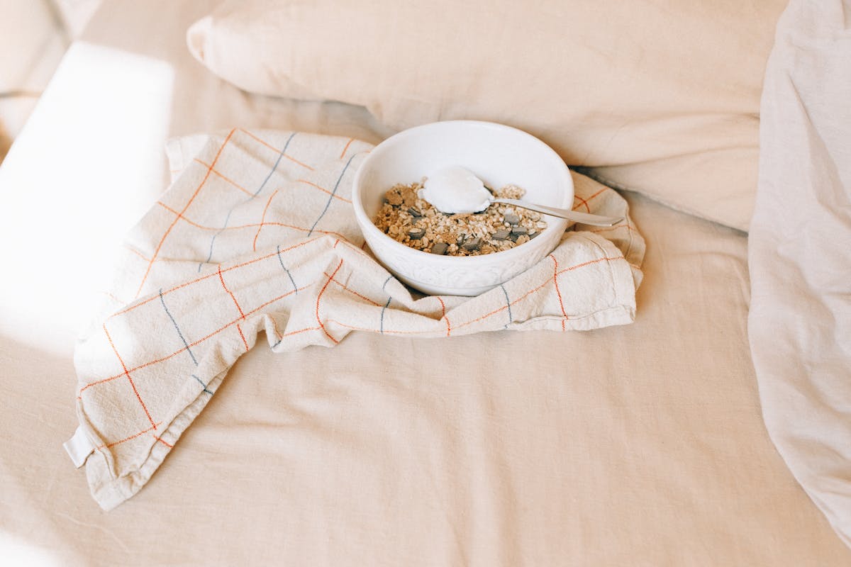 8 Worst Foods to Eat Before Bed That Quietly Destroy a Good Night’s Sleep 2 A bowl of granola with yogurt on a bed, exuding a cozy morning ambiance.