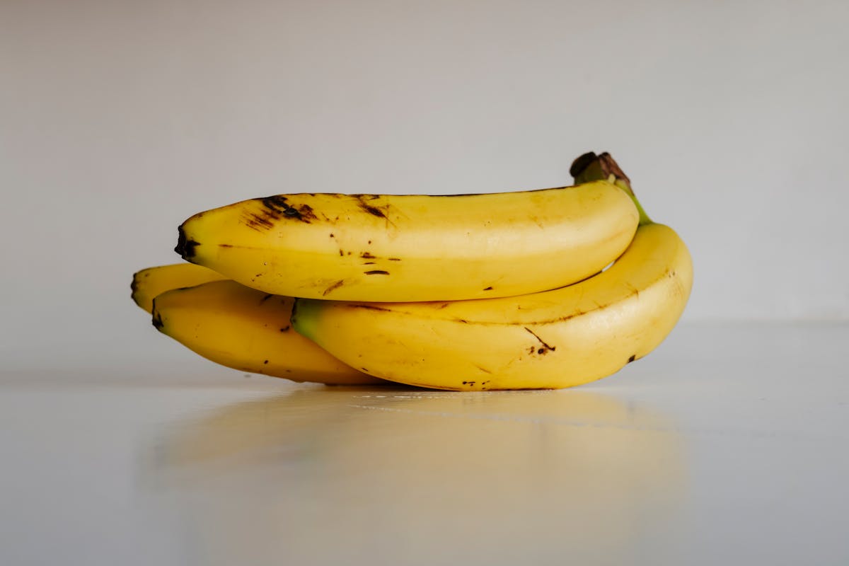 9 Shocking Dark Stories About Bananas 2 A bunch of fresh yellow bananas stacked elegantly on a smooth white surface, ready to eat.